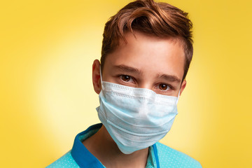 The concept of protection against viruses and diseases. Close-up portrait of a teenage boy in a blue t-shirt and mask. Yellow background. Copy space