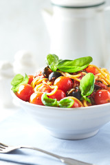 Spaghetti pasta with cherry tomatoes, black olives and fresh basil in a small bowl. Bright background