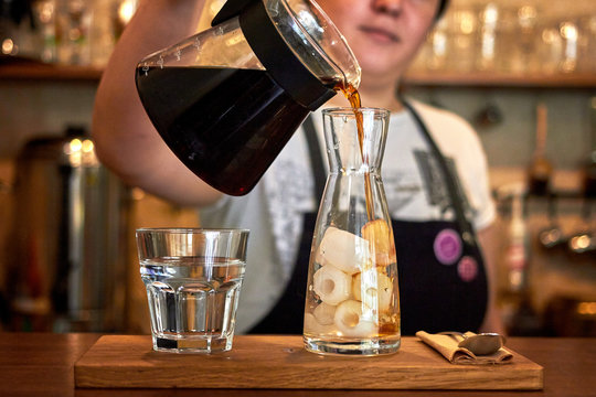 Pours coffee in a glass jar with ice. Barista woman prepares cold brew coffee in glass bottle in the coffee shop