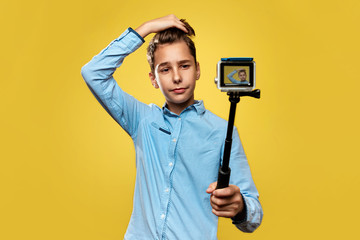 Beautiful boy blogger makes a selfie or video on a compact camera with the monopod. Yellow...
