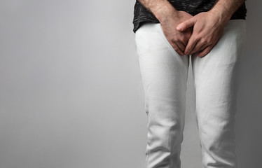 The man in white jeans folded his hands at the level of his genitals. Disease for men. The concept...