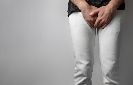 The man in white jeans folded his hands at the level of his genitals. Disease for men. The concept of protection against sexually transmitted infections. Copy space