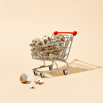 Quail eggs in a shopping cart and broken shells on a beige background with copy space. Concept of financial loss
