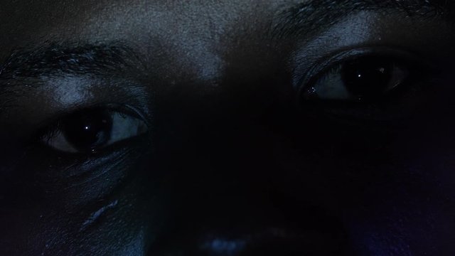 black man's eyes watching TV alone in the dark