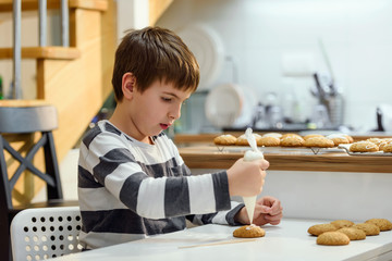 Fototapeta na wymiar Cute boy decorating holiday gingerbread cookies at home kitchen