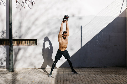 Young sportive man training with kettlebell near grey wall