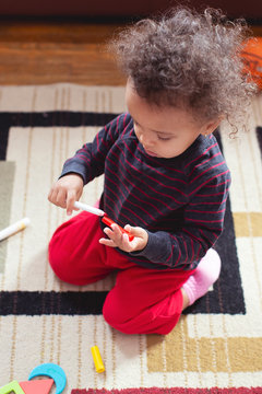 Pretty mixed toddler child with wild curly hair recapping a red marker