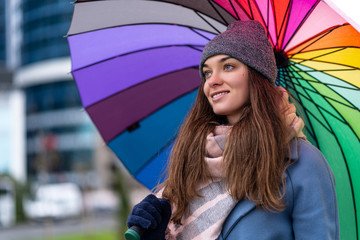 Portrait of happy smiling joyful carefree woman in warm clothes with bright multicolored rainbow...