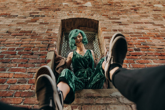 Beautiful woman laughing with green hair sitting on a ledge of a brick wall building outside in the city