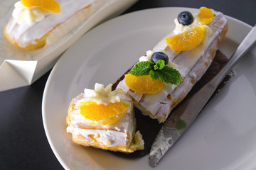 Cake with cream and fresh fruits on a white plate. Blueberry, tangerine slices and mint leaves. The cake is cut. The knife smeared in the cream lies on the plate.