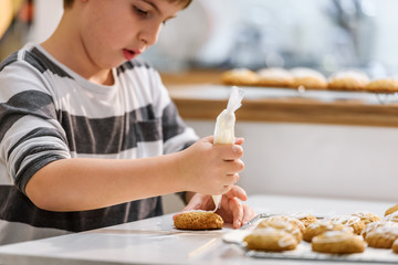 Cute boy decorating holiday gingerbread cookies at home kitchen