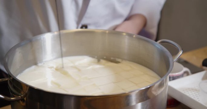 Cheesemaker making cheese. Stirs the curdled milk.
