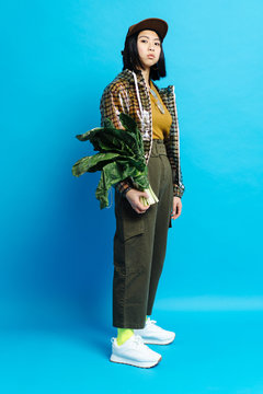 Young serious stylish lady in cap with bunch of plants