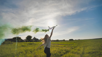 A young girl with a toy airplane smokes colorful smoke on a summer evening.