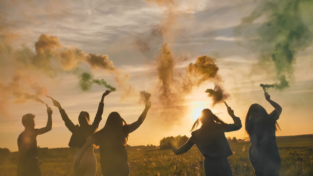 Happy friends girls waving colorful smoke at sunset.