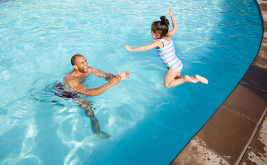 African American father playing with daughter in swimming pool