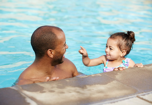 Ethnic father playing with his young daughter in a swimming pool
