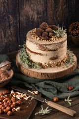 Delicious naked chocolate and hazelnuts cake on table rustic wood kitchen countertop.