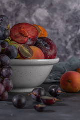 Fruits Still life with fruit on whte ceramic bowl. Concrete wall. Dramatic light. Grapes, apricots and plums.
