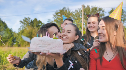 Happy friends celebrate their girlfriend's birthday. The birthday girl blows out the candles.
