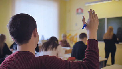 Naklejka na ściany i meble High school student raises his hand during the lesson.