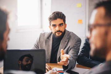 Young Caucasian dedicated executive presenting his plans and ideas to team members while sitting in the office.