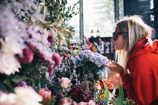 Pretty young lady with sunglasses walks smells flowers at florist in Sydney.