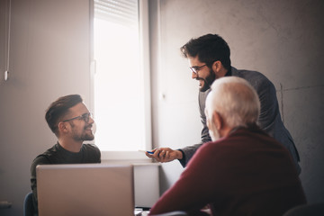 Two young and one senior bearded Caucasian businessmen discussing their ideas and strategies while they are sitting in the office.