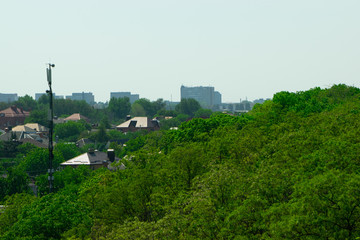 Obraz premium The repeater tower rises above the green crowns of trees against the background of houses in the distance