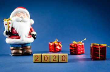 Blue christmas background with Santa Clause figure and gifts in a conceptual image with 2020 spelled on gold blocks.