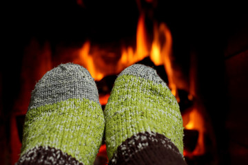 A woman warms her feet in knitted socks by the fireplace on a winter evening