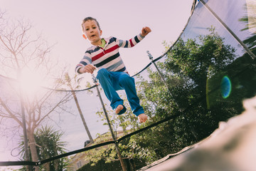 5 year old boy jumping on a trampoline exercising in the backyard of his house, enjoying the spring with gesture of happiness and lifestyle.