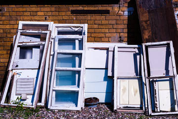 old broken windows that stand on a wall, many old and broken windows, standing on ground