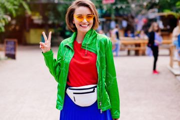 Portrait of beautiful smiling brunette model dressed in summer hipster jacket clothes. Trendy girl posing in the street background. Funny and positive woman in round sunglasses.