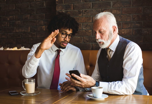 A young employee presenting the new data compiling software to his senior manager in a pleasant indoor atmosphere. The two people are drinking coffee.