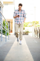 Full length happy young man walking with mobile phone outside