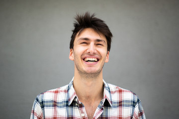 Close up of happy young man laughing by gray background and looking up