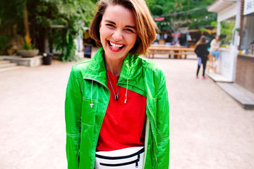 Portrait of beautiful smiling hipster model dressed in summer colourful  clothes. Trendy girl posing in the street background. Funny and positive woman having fun.Shows tongue and winking