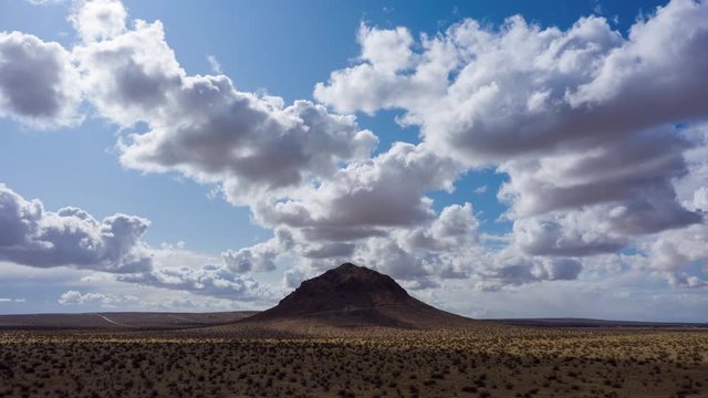 Aerial hyperlapse flying toward Mojave Desert butte with fluffy clouds