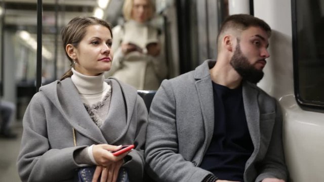 Positive bearded guy enjoying friendly conversation with young woman while traveling on subway train