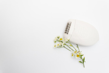 White electric epilator to remove unwanted hair. Beauty and skin care concept. Healing daisy flower