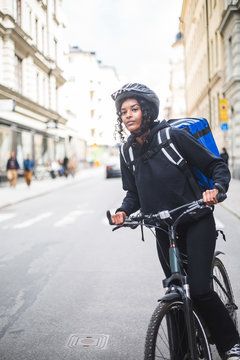 Delivery woman looking away while standing with bicycle on street in city