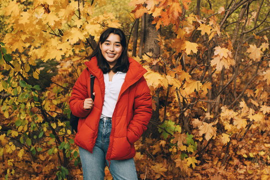 Portrait of smiling teenage girl standing with backpack against autumn trees