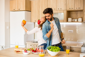 A yong couple dancing and air miking while preparing a meal in the kitchen. There are various colorful vegetables.