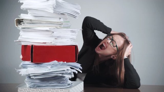 A pile of unfilled documentation on desk in the office, stressed office worker screaming in anger and tearing her hair being disappointed. Furious office manager, nervous breakdown, stress management