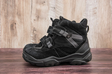 black, children's boots on a wooden background. Side view