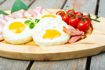 Tasty fried eggs with vegetables on a wooden plate.