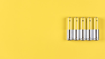 Photo of five gray-yellow alkaline AA batteries on a yellow background. Recycling of rechargeable...