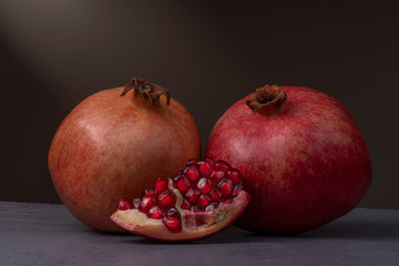 Two ripe pomegranate fruits and one slice of pomegranate on a wooden surface