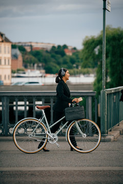 Side view of businesswoman walking with bicycle on bridge in city
